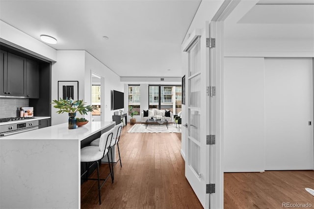 kitchen featuring stainless steel oven, gas stovetop, hardwood / wood-style flooring, a kitchen breakfast bar, and backsplash