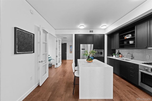 kitchen featuring a kitchen island, stainless steel appliances, sink, backsplash, and a breakfast bar area