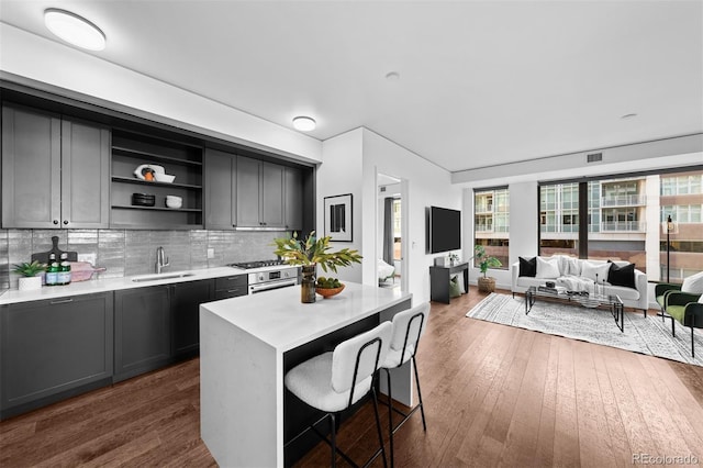 kitchen with decorative backsplash, sink, a kitchen island, dark wood-type flooring, and a breakfast bar