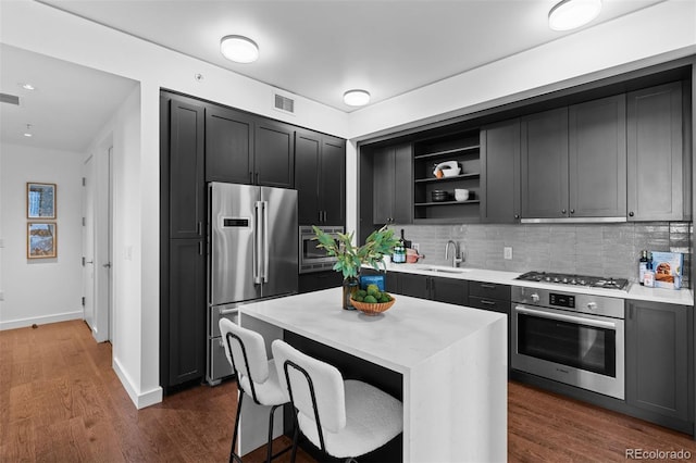 kitchen featuring sink, backsplash, dark wood-type flooring, a center island, and stainless steel appliances