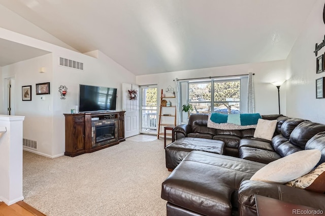 living room featuring light colored carpet, visible vents, vaulted ceiling, and a glass covered fireplace