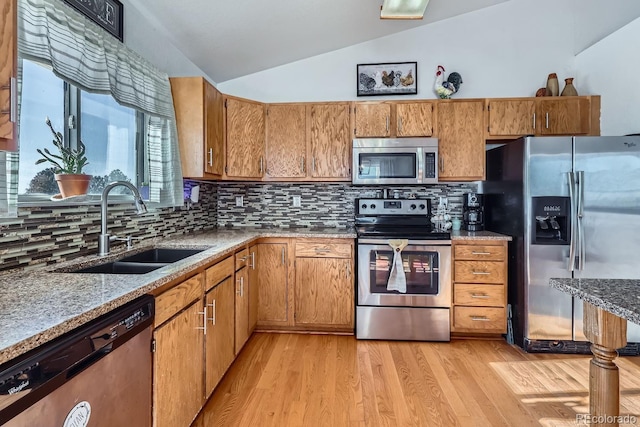 kitchen featuring lofted ceiling, appliances with stainless steel finishes, brown cabinetry, and a sink