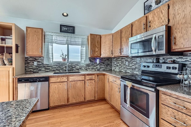 kitchen featuring lofted ceiling, light wood-style flooring, a sink, appliances with stainless steel finishes, and backsplash