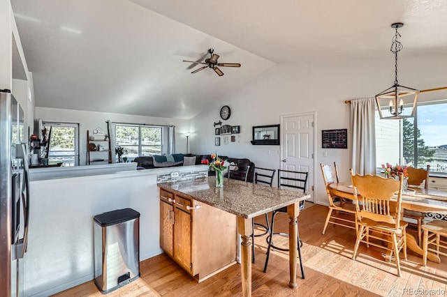 kitchen with light wood finished floors, dark stone counters, open floor plan, a peninsula, and hanging light fixtures