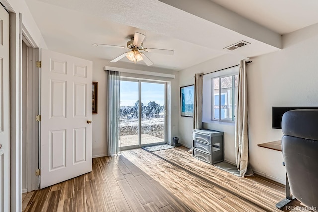 unfurnished office featuring visible vents, a ceiling fan, a wood stove, wood finished floors, and baseboards