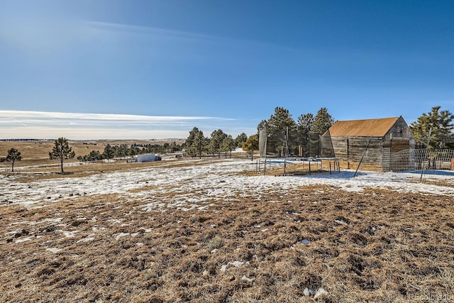 yard covered in snow featuring a trampoline, fence, an outbuilding, and a rural view