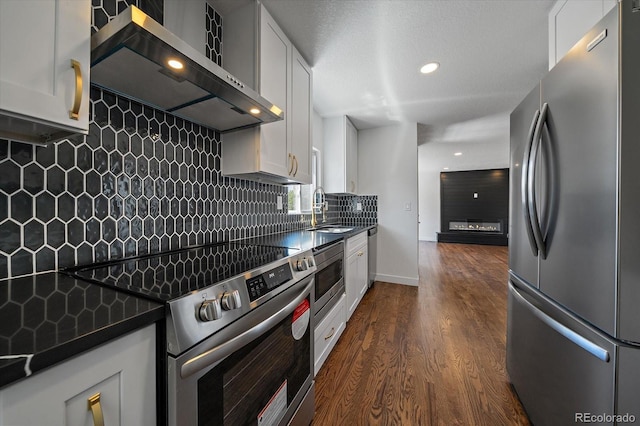 716 S Osage, Denver, CO 80223 - kitchen featuring stainless steel appliances, wall chimney range hood, dark countertops, a sink, and recessed lighting