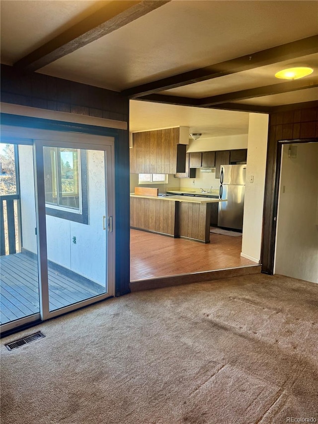 kitchen with beamed ceiling, light colored carpet, and stainless steel refrigerator