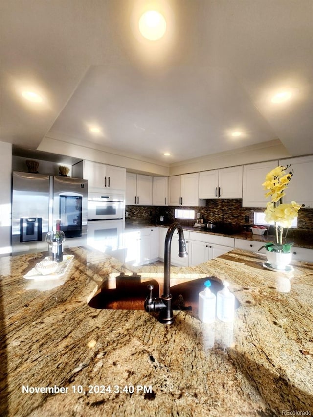 kitchen featuring white cabinetry, sink, stainless steel fridge, oven, and stone countertops