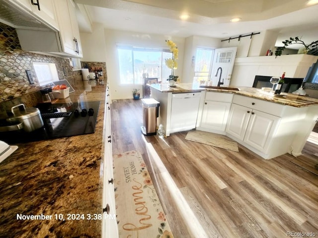 kitchen featuring sink, dishwasher, kitchen peninsula, white cabinets, and light wood-type flooring