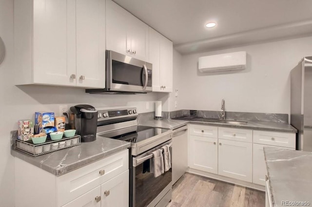 kitchen featuring sink, appliances with stainless steel finishes, stainless steel counters, white cabinetry, and a wall unit AC