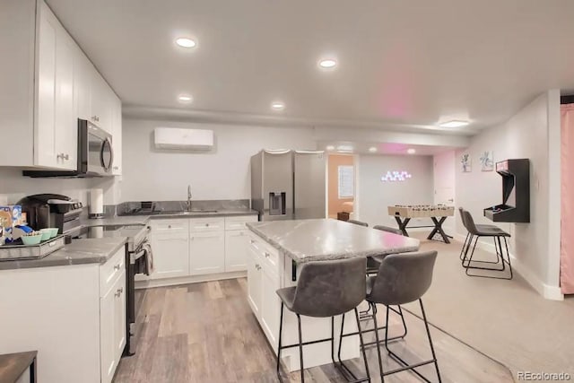 kitchen featuring stainless steel appliances, a wall unit AC, sink, a center island, and white cabinetry