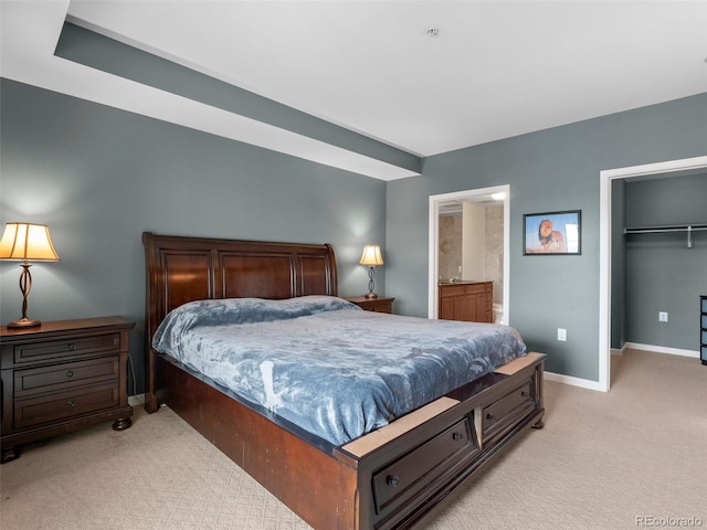 bedroom featuring baseboards, a closet, light carpet, a walk in closet, and connected bathroom