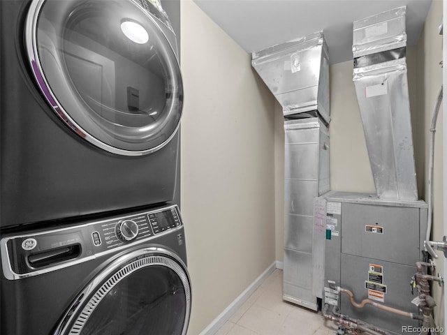 laundry room with heating unit, light tile patterned floors, baseboards, stacked washing maching and dryer, and laundry area