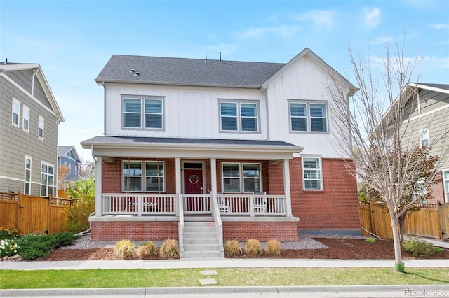 view of front of house with board and batten siding, brick siding, fence, and covered porch