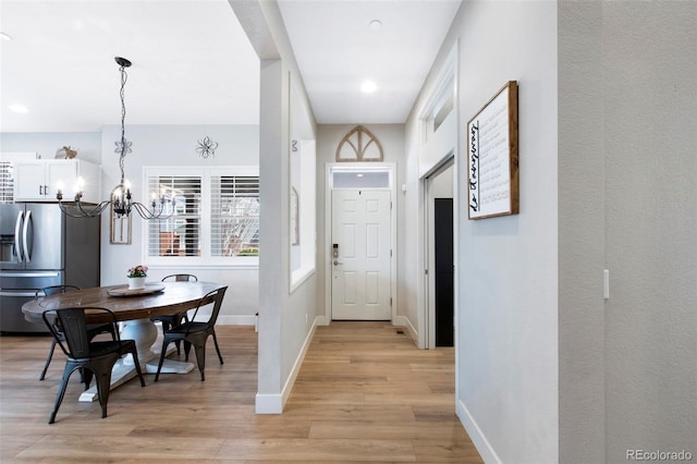 doorway to outside featuring baseboards, light wood-type flooring, and a notable chandelier