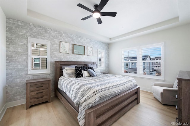 bedroom featuring multiple windows, light wood-style flooring, and a raised ceiling