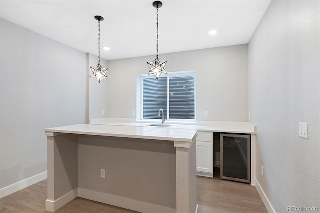 kitchen featuring a sink, beverage cooler, white cabinetry, baseboards, and decorative light fixtures