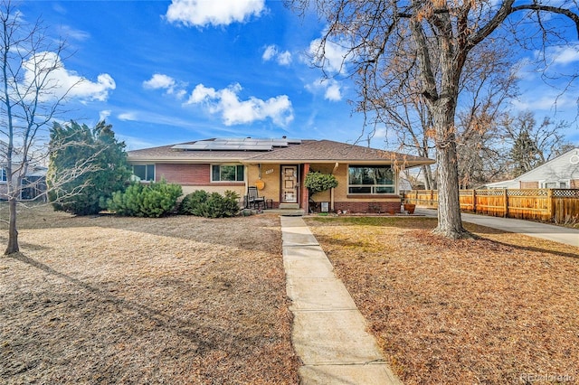 view of front of house featuring fence, solar panels, and brick siding