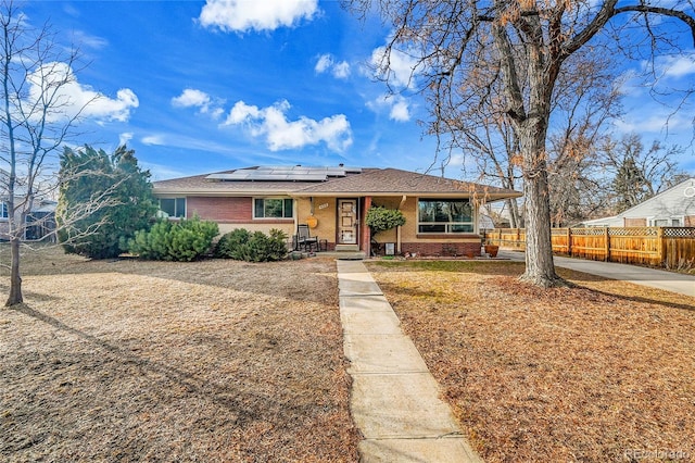 view of front of home featuring fence, solar panels, and brick siding