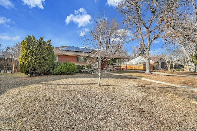 single story home featuring brick siding, fence, and roof mounted solar panels