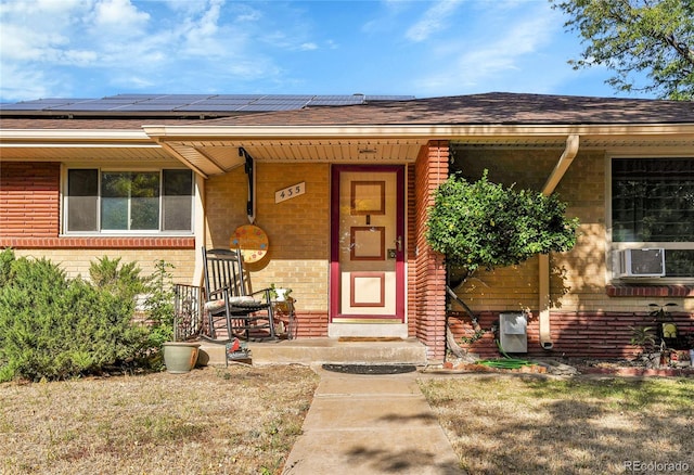 view of exterior entry with solar panels, roof with shingles, cooling unit, and brick siding