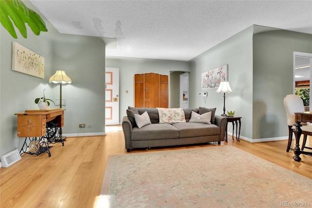 living area with a textured ceiling, wood finished floors, visible vents, and baseboards