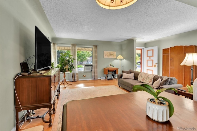 living area with cooling unit, a textured ceiling, baseboards, and wood finished floors