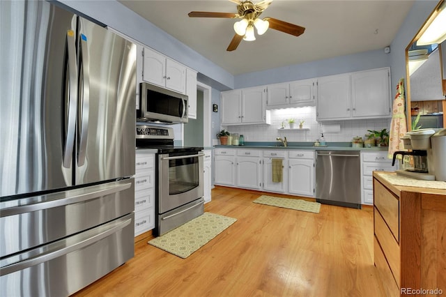 kitchen with white cabinets, light wood-style flooring, stainless steel appliances, and backsplash