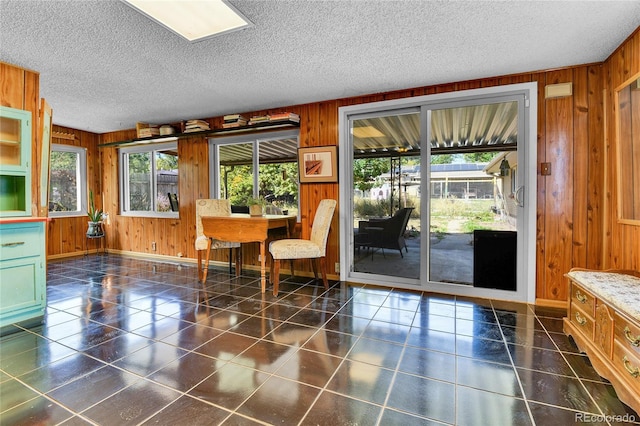 tiled dining space with wood walls, a textured ceiling, and baseboards