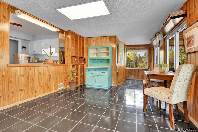 interior space with visible vents, wooden walls, a textured ceiling, dark tile patterned flooring, and stainless steel fridge