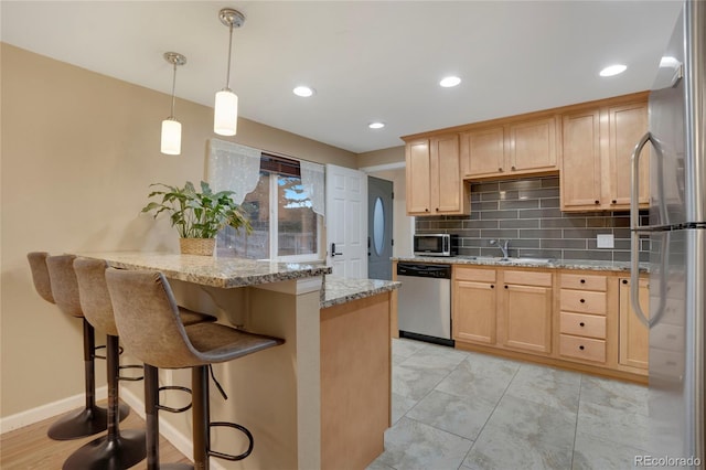 kitchen featuring decorative backsplash, appliances with stainless steel finishes, light brown cabinets, a sink, and a kitchen bar