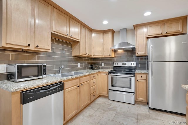 kitchen with stainless steel appliances, light brown cabinets, a sink, and wall chimney range hood