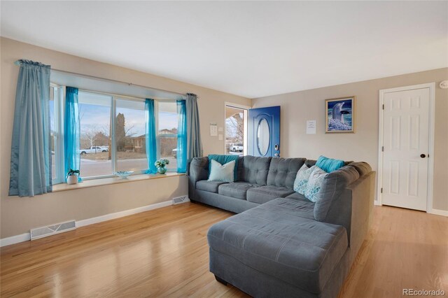 living room featuring visible vents, light wood-style flooring, and baseboards