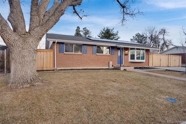 single story home featuring a front yard, roof mounted solar panels, brick siding, and fence