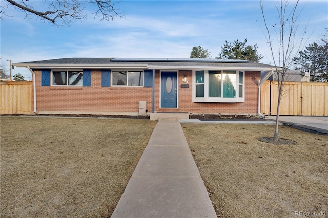 view of front facade with brick siding, a front lawn, fence, and roof mounted solar panels