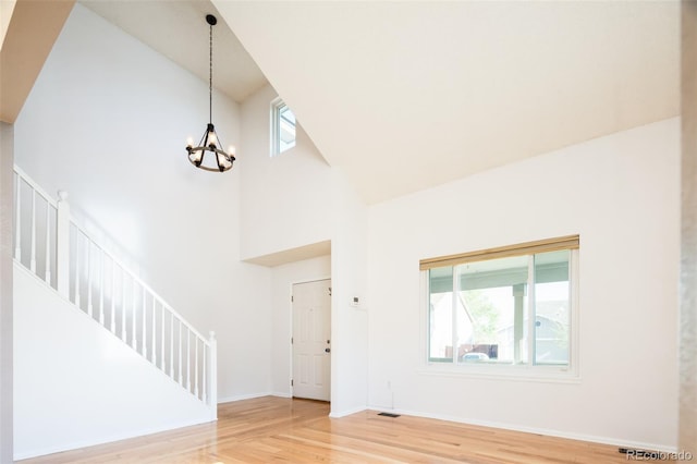 foyer entrance featuring an inviting chandelier, wood finished floors, baseboards, high vaulted ceiling, and stairway