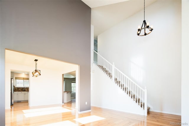 unfurnished living room featuring plenty of natural light, light wood finished floors, a chandelier, a high ceiling, and stairs