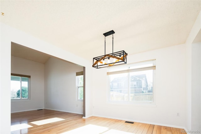 spare room featuring a chandelier, plenty of natural light, visible vents, and light wood-style floors