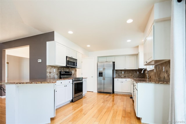 kitchen featuring a sink, light wood-type flooring, stainless steel appliances, and dark stone countertops