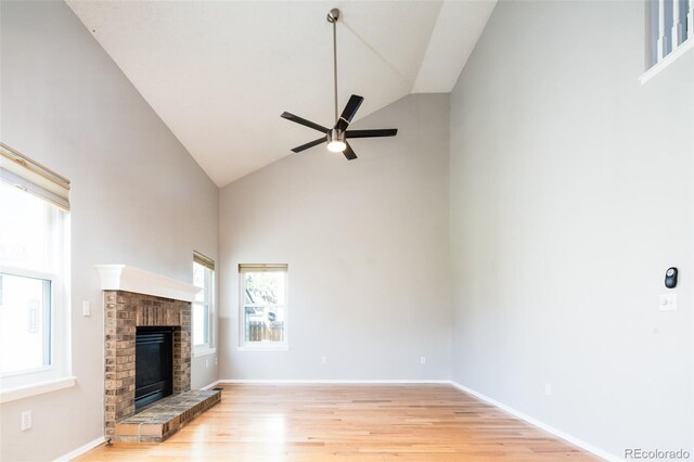 unfurnished living room featuring ceiling fan, a brick fireplace, light wood-type flooring, high vaulted ceiling, and baseboards