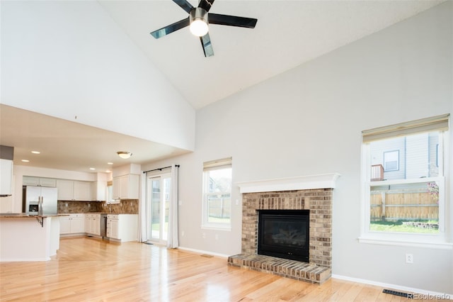 unfurnished living room with visible vents, a healthy amount of sunlight, ceiling fan, high vaulted ceiling, and light wood-style flooring