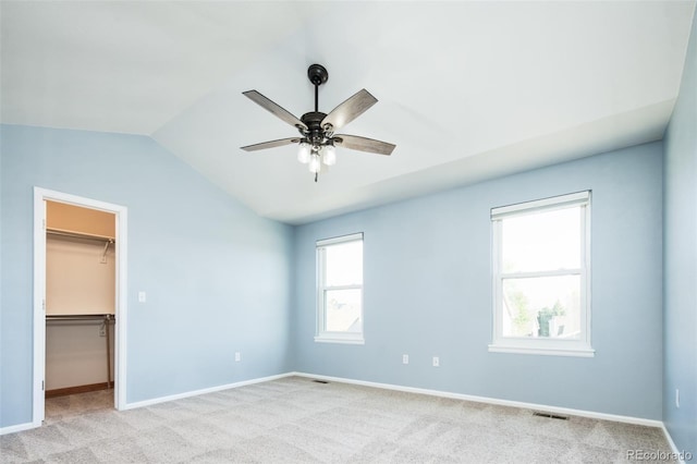 unfurnished bedroom featuring light colored carpet, baseboards, a spacious closet, and lofted ceiling
