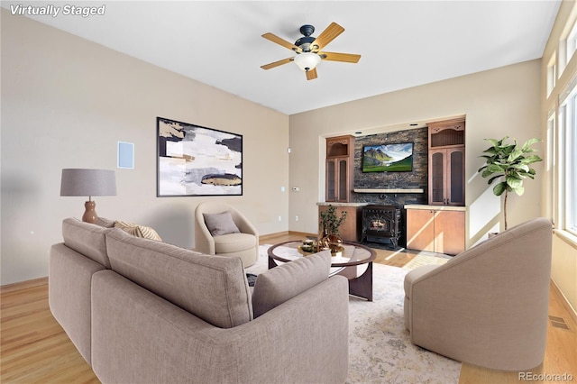 living room with ceiling fan, light hardwood / wood-style floors, and a wood stove