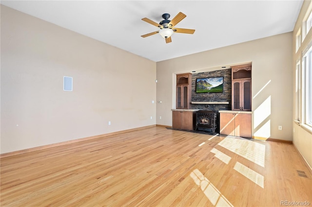 unfurnished living room featuring ceiling fan, light hardwood / wood-style floors, and a wood stove