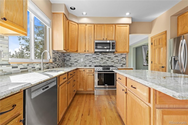 kitchen with sink, light stone counters, light wood-type flooring, appliances with stainless steel finishes, and decorative backsplash