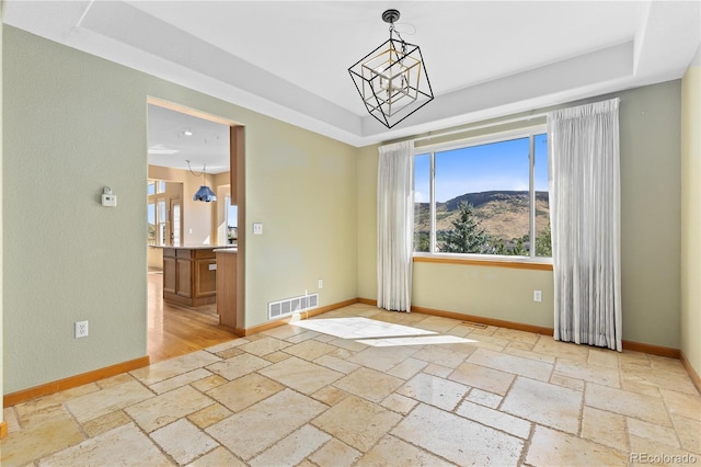 empty room with a raised ceiling, a mountain view, and an inviting chandelier