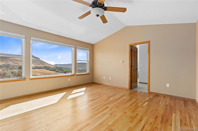 empty room with vaulted ceiling, a mountain view, ceiling fan, and light wood-type flooring