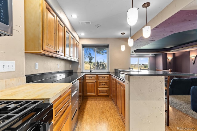 kitchen featuring hanging light fixtures, gas range oven, a kitchen bar, and light hardwood / wood-style floors