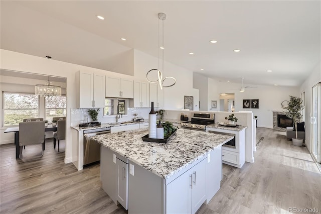 kitchen featuring white cabinetry, a center island, stainless steel appliances, lofted ceiling, and decorative light fixtures